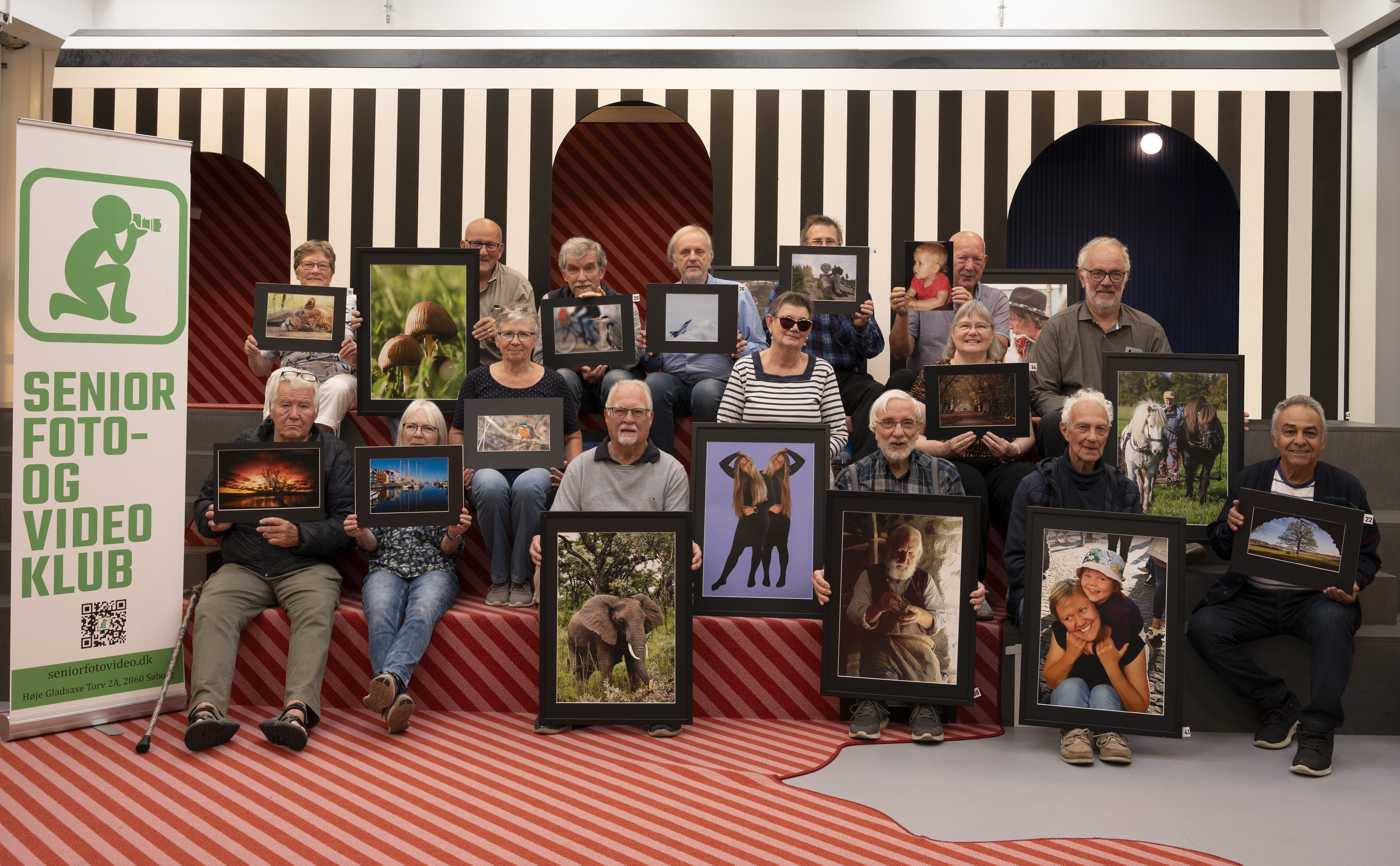 Medlemmerne i Seniorfoto- og Videoklubben sidder på en trappe og holder hver et billede foran sig